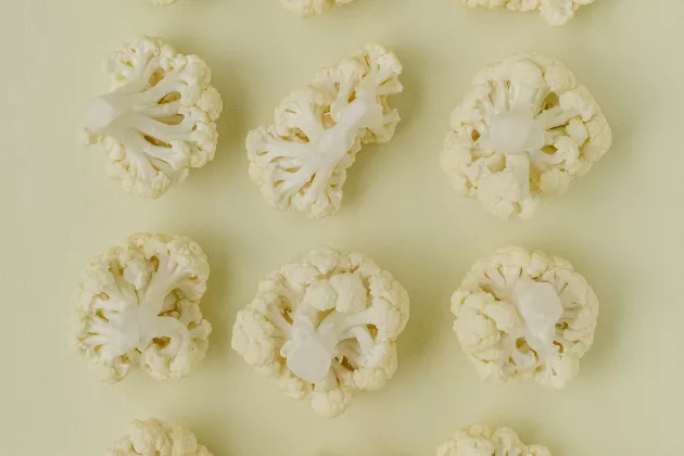Photo of cauliflower heads in different shapes on a pale yellow background.