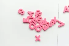 Photo: A close-up of several pink letters in a pile against a white background.