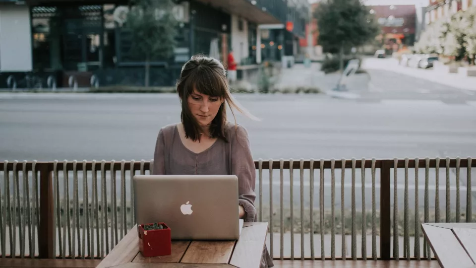 Bild som visar person som sitter utomhus framför en bärbar dator