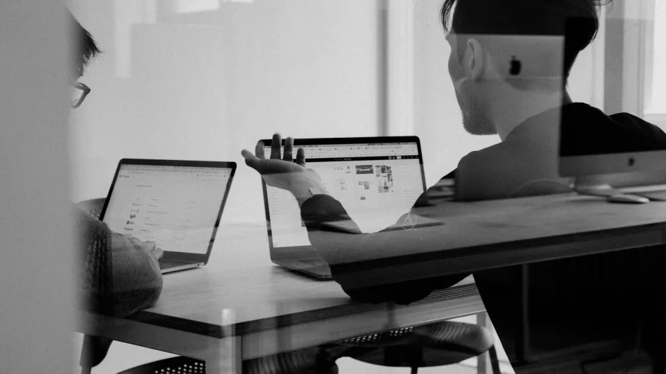 Foto genom en glasruta som visar två personer som samtalar med två bärbara datorer framför sig.