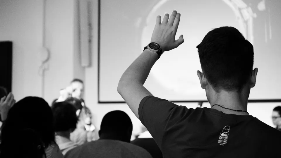 Foto från ett klassrum med en student som räcker upp handen.