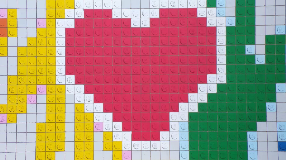 Foto som visar färgglada legobitar som bildar ett rött hjärta och två händer som möts.