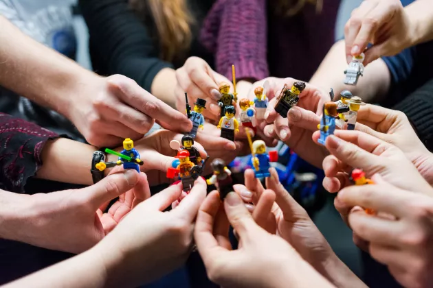 Foto av ett antal händer i en ringformation som håller i olika LEGO-figurer.