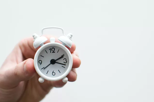 Bild som visar en hand som håller i en liten vit väckarklocka i metall.