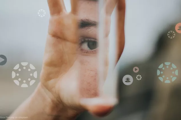 En hand som håller i en skärva från en spegel där ett mänskligt öga syns.