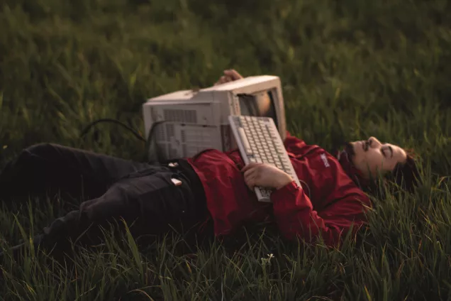 En person som ligger i gräset med en dator av äldre modell på magen.