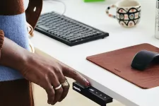 Foto på en hand som trycker på en knapp på ett höj- och sänkbart skrivbord.