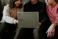 Foto av tre personer som sitter ner tillsammans och pratar med en bärbar dator mellan sig i knät.
