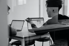 Foto genom en glasruta som visar två personer som samtalar med två bärbara datorer framför sig.